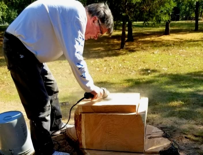 Tom Rogers carves and sands a chess board into a stump at Slater Park.